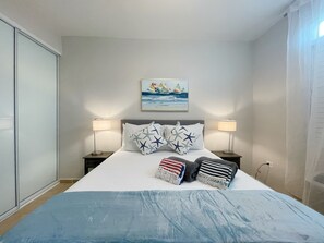 A hotel room with a bed, two bedside lamps, a painting of sailboats, and a view of the sea. - Palmas del Mar Family Vacation Resort Spot!   (Palmas del Mar)