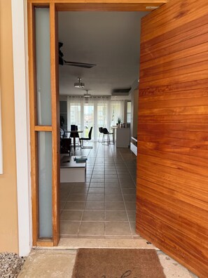 Eine offene Tür führt in ein Wohnzimmer mit Essbereich, einer Küche und Blick ins Freie.