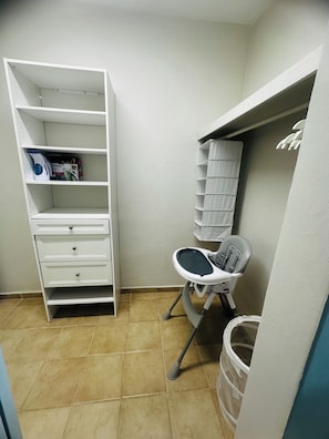 A small, clean room with a white shelving unit, a baby changing station, and a trash bin.