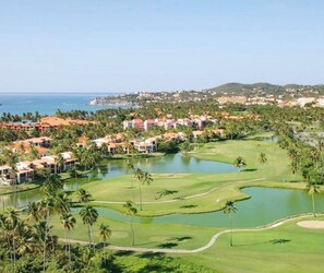 A golf course with a water hazard, surrounded by palm trees and buildings. - Palmas del Mar Family Vacation Resort Spot!   (Palmas del Mar)