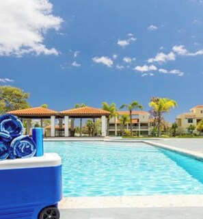 A swimming pool with a clear blue sky, a covered area with a roof, and a building with a red-tiled roof in the background. - Palmas del Mar Family Vacation Resort Spot!   (Palmas del Mar)