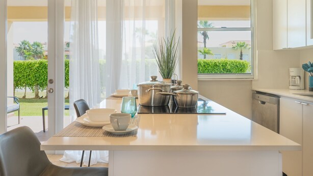 A modern kitchen with a central island, a dining area with chairs, and a view of a garden through the window. - Palmas del Mar Family Vacation Resort Spot!   (Palmas del Mar)