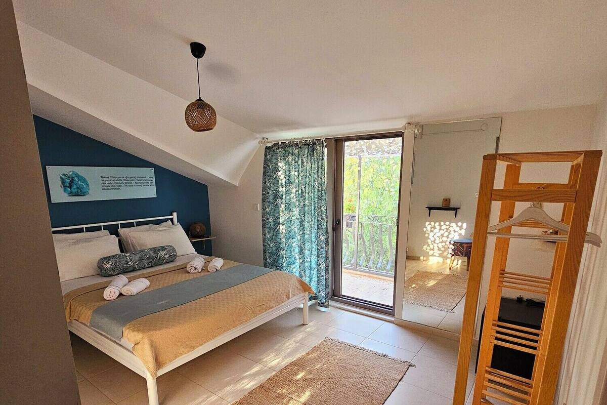 A bedroom with a bed, a blue chair, a wooden ladder, and a view of the outdoors.