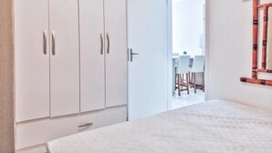 A bedroom with a bed, a wardrobe, and a door leading to a balcony with a table and chairs. - Ap Centro no Coração de BC - 500m do Mar (Balneário Camboriú)