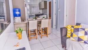 A compact living space with a kitchenette, a dining area, and a sofa with patterned cushions. - Ap Centro no Coração de BC - 500m do Mar (Balneário Camboriú)