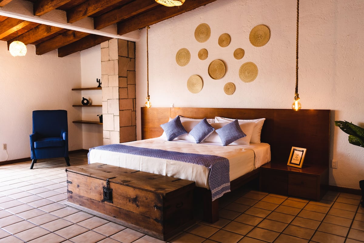A bedroom with a wooden headboard, a bed with blue and white bedding, a chest of drawers, a blue chair, and a wall with circular decorations.