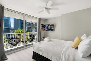 Ein Hotelzimmer mit großem Balkon, einem Bett mit weißer Bettwäsche, einem Deckenventilator und einer Wandcollage mit Fotos.