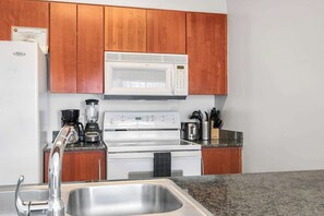 A kitchen with wooden cabinets, a white microwave, a stove, a coffee maker, and a sink.