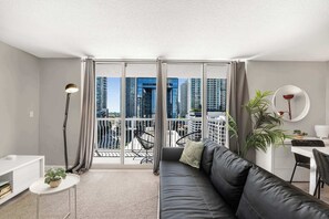 Ein modernes Wohnzimmer mit einer schwarzen Ledersofa, einem kleinen weißen Tisch mit Pflanze, einer Stehlampe und einem Essbereich mit Spiegel und Pflanze.