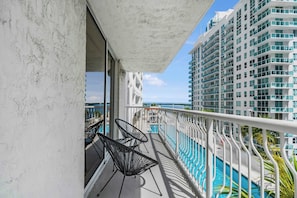 A balcony with two black chairs, a pool, and a view of a high-rise building.