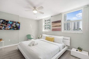 Ein modernes Schlafzimmer mit Bett, Deckenventilator, Fenster mit Stadtblick und einer Wandcollage.