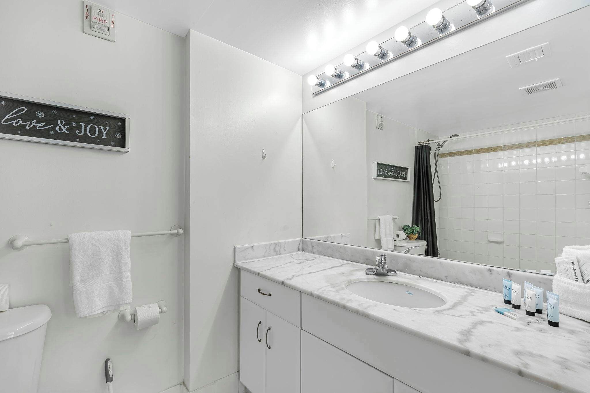 A modern bathroom with a vanity, a large mirror, and a sign that reads "love & joy".