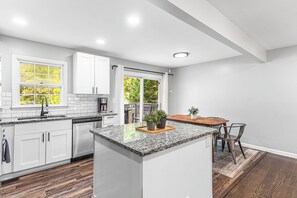 A modern kitchen with white cabinets, a granite countertop, and a wooden dining table.