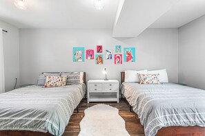 A bedroom with two beds, a white nightstand, a rug, and colorful artwork on the wall.