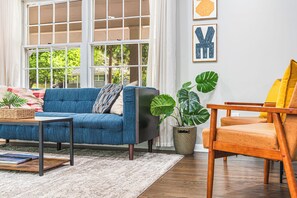 A living room with a blue sofa, a wooden chair, a coffee table, and a potted plant.