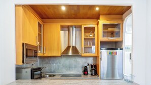 Eine kompakte Küche mit Holzausstattung, einer Edelstahl-Dunstabzugshaube, einer eingebauten Mikrowelle und einem Kühlschrank mit digitaler Anzeige.