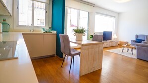 A modern kitchen with a central island, a dining area with a grey sofa and a small table, and a living area with a blue armchair and a grey sofa. - Elite Bonaire Penthouse by Hello Homes Sitges (Sitges)