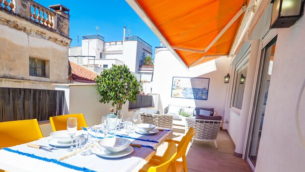 An outdoor dining area with yellow chairs and a table set for two, under an orange canopy. - Elite Bonaire Penthouse by Hello Homes Sitges (Sitges)
