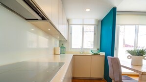 A modern kitchen with a central island, a dining area with a chair, and a view of the outside through large windows. - Elite Bonaire Penthouse by Hello Homes Sitges (Sitges)