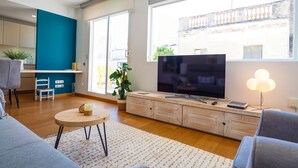 A modern living room with a large TV, a sofa, a small table, and a potted plant. - Elite Bonaire Penthouse by Hello Homes Sitges (Sitges)