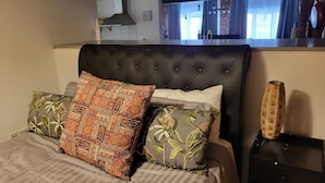 A bedroom with a tufted headboard, a bed with striped bedding, and two decorative pillows with tropical patterns. - Captivating 2-bed Apartment in Liverpool (Liverpool)