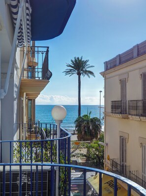 Un balcón con vista al mar, una palmera y un edificio con balcón.