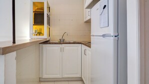 Cozinha compacta com armários brancos, pia de aço inoxidável e geladeira embutida.