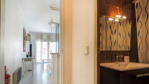 Un pasillo que conduce a un baño con lavamanos y cortina de ducha con estampado ondulado.