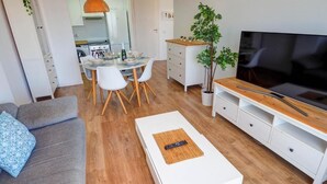 A modern living room with a sofa, coffee table, TV stand, dining area, and kitchen in the background. - Apartment by the Sea by Hello Homes Sitges (Sitges)