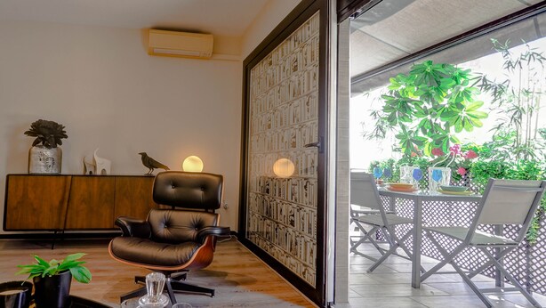 A modern living room with a leather chair, a wooden cabinet, and a glass table with drinks. - Flamingo Apartment by Hello Homes Sitges (Sitges)