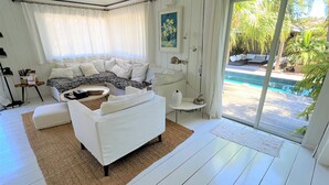 En moderne stue med en hvid sofa, et sofabord og udsigt til en swimmingpool.