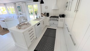 Et moderne køkken med hvide skabe, en central ø, hængende sort lamper og en tæppe med mønster.