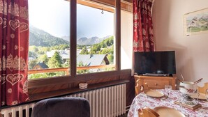A cozy room with a large window, a wooden table set for dining, a chair, a television, and a radiator. - 2-room south-facing apartment with balcony and parking (Valloire)
