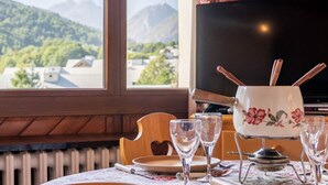 A dining table with a view of mountains through a window, a television, and a floral-patterned tablecloth. - 2-room south-facing apartment with balcony and parking (Valloire)