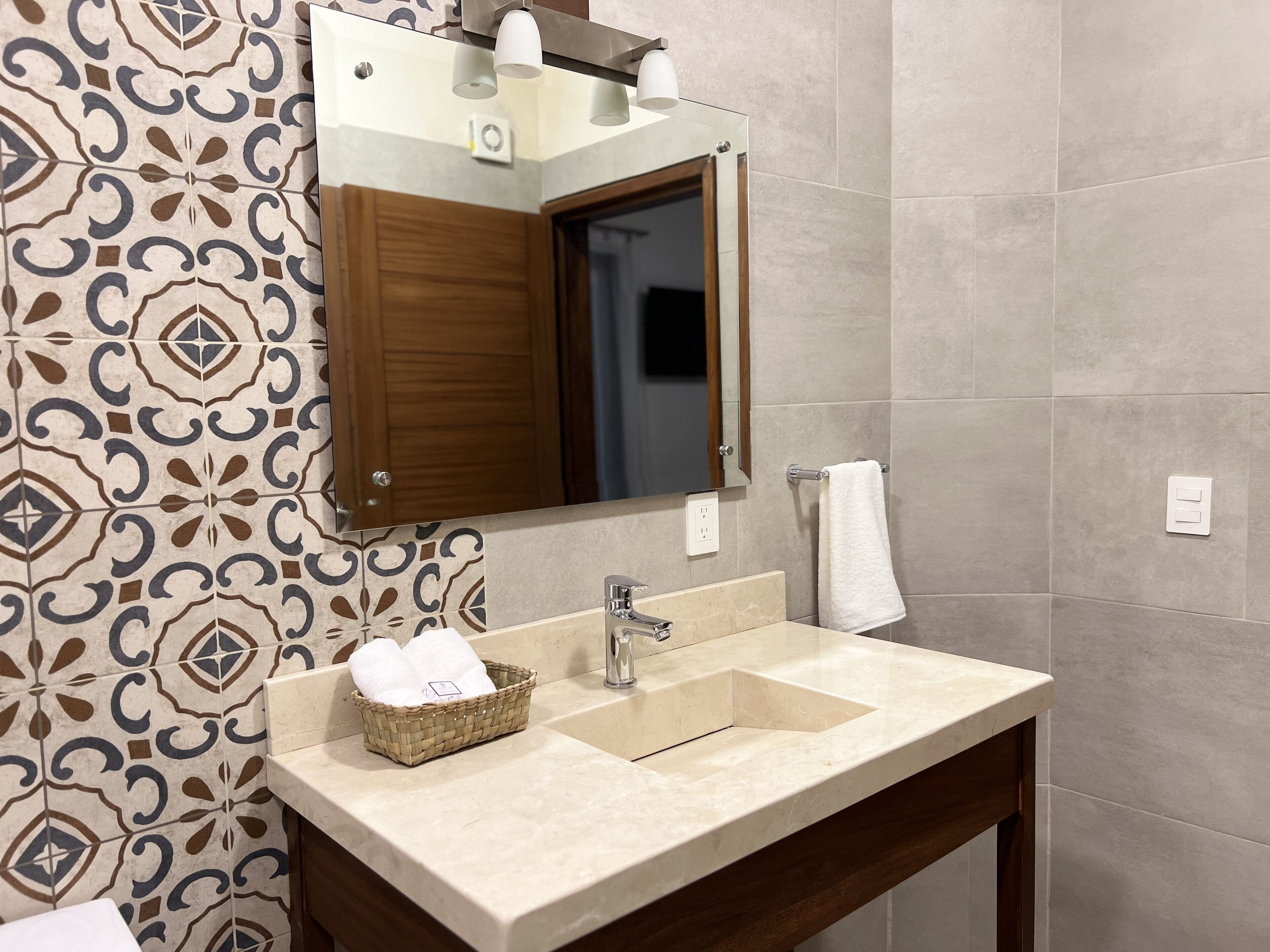 A bathroom with patterned tiles, a wooden-framed mirror, a beige sink, and a towel hanging on a rack.