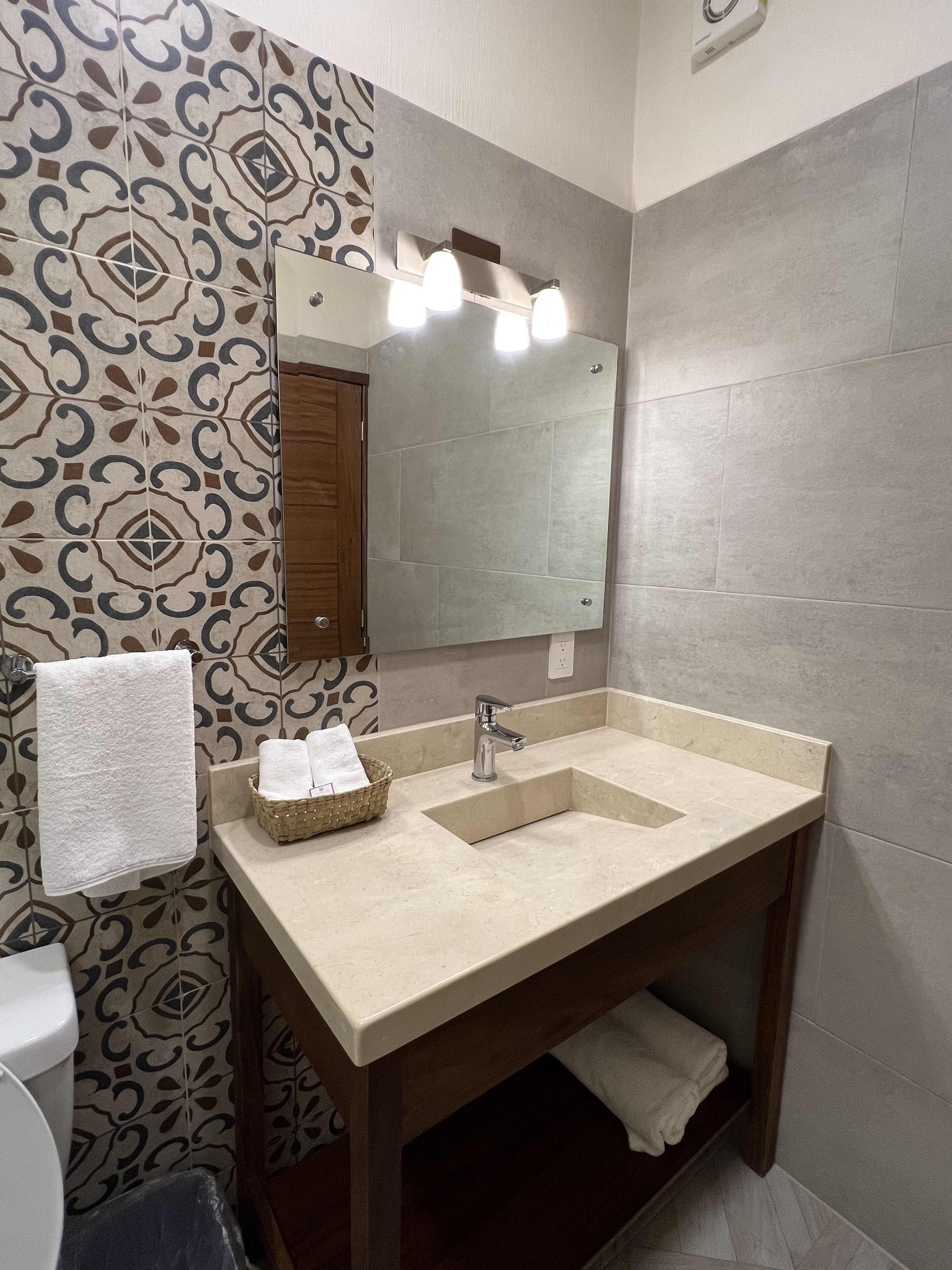 Un baño con pared de baldosas estampadas, un lavamanos con espejo y un perchero para toallas.
