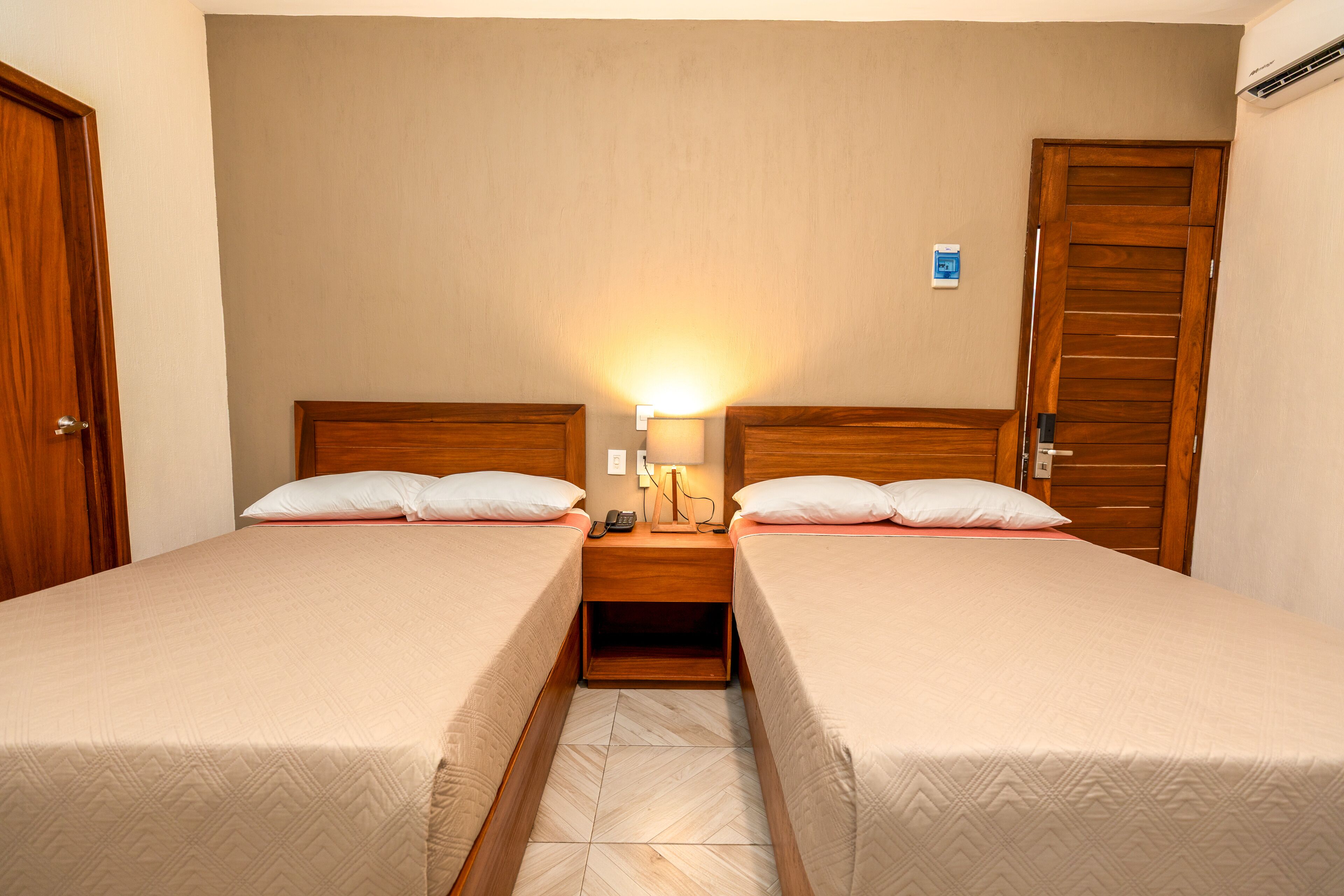 A hotel room with two single beds, a nightstand with a lamp, and a wooden wardrobe.