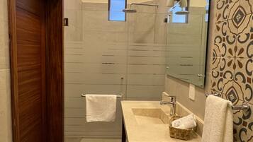 Un baño moderno con puerta de madera, un espejo grande, un lavamanos con toalla y zona de ducha.