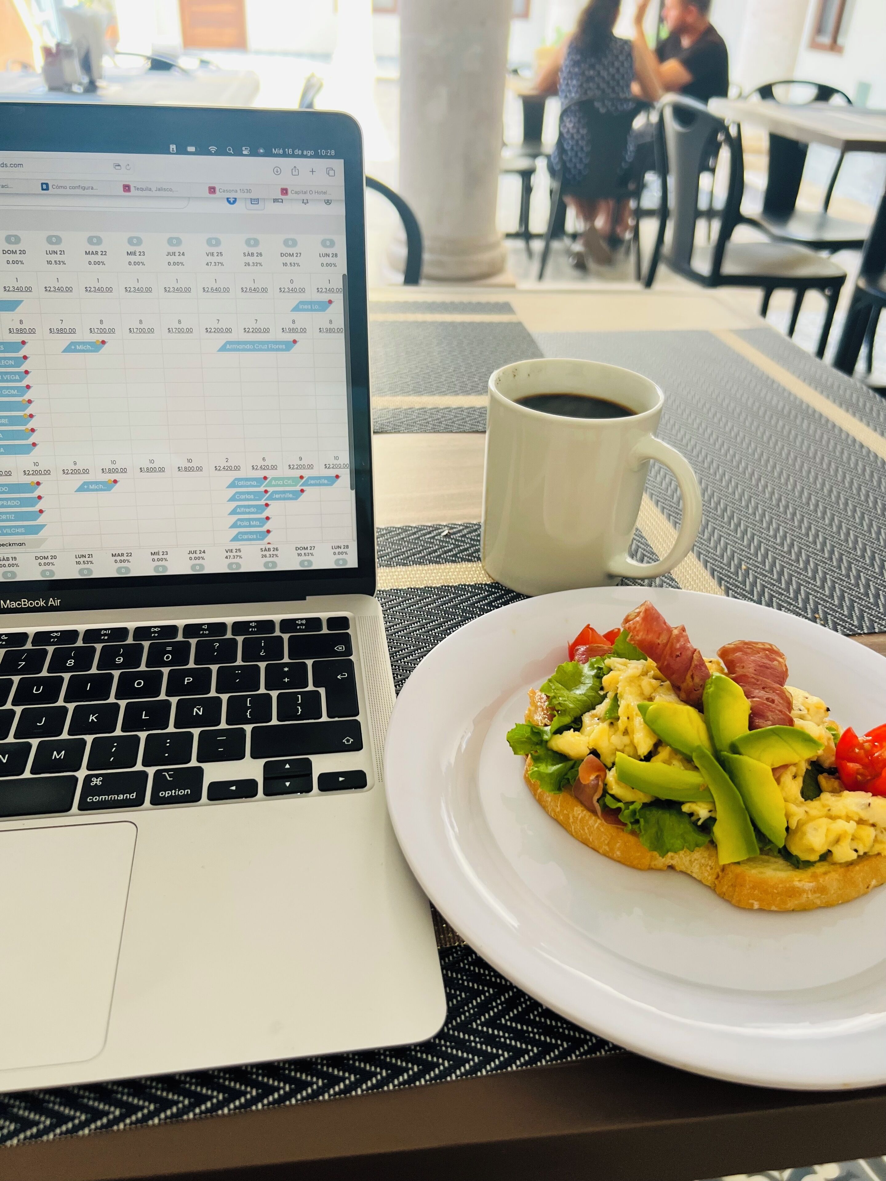 Una computadora portátil sobre una mesa, con una taza de café y un plato de comida.