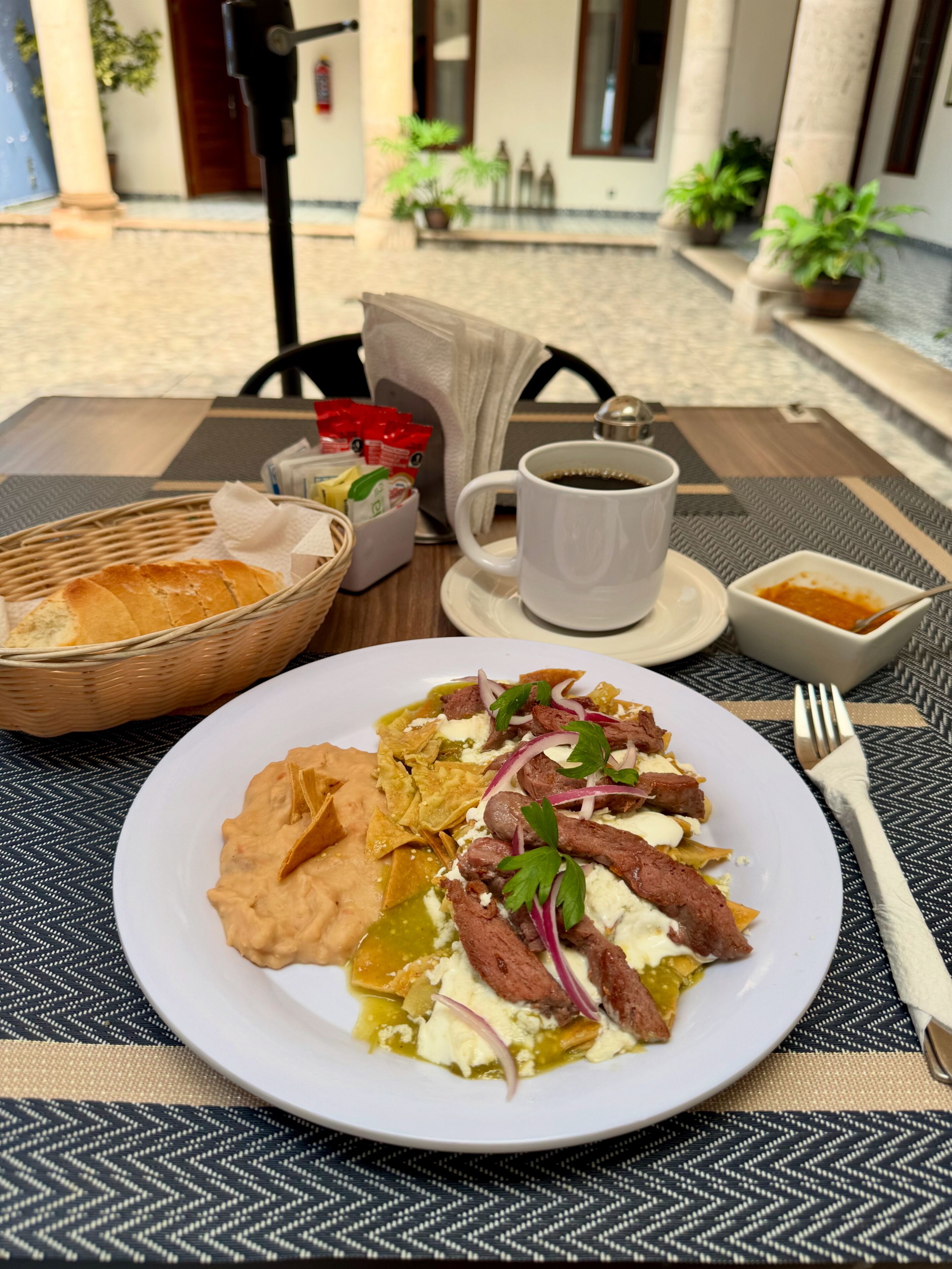 Une table à manger avec une assiette de nourriture, une tasse de café et un panier de pain.