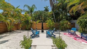 A backyard with two blue lounge chairs, a red and white patterned rug, and various tropical plants. - The Ivanhoe Getaway (Sarasota)