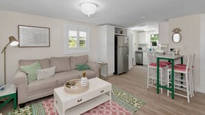 A modern living room with a sofa, coffee table, and a dining area with chairs. - The Ivanhoe Getaway (Sarasota)