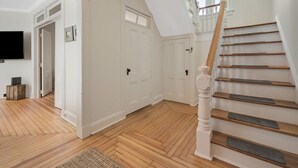 Una habitación amplia con piso de madera, paredes blancas y una escalera de madera con barandilla blanca.