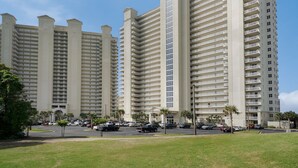 A multi-story hotel with a uniform facade, multiple balconies, and a parking area with cars. -  Ariel Dunes l - Its Tannin' Time! - Fantastic Gulf Views! (Miramar Beach)