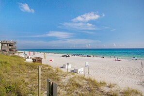 Una playa con un edificio de varios niveles, sombrillas y un cielo azul despejado.