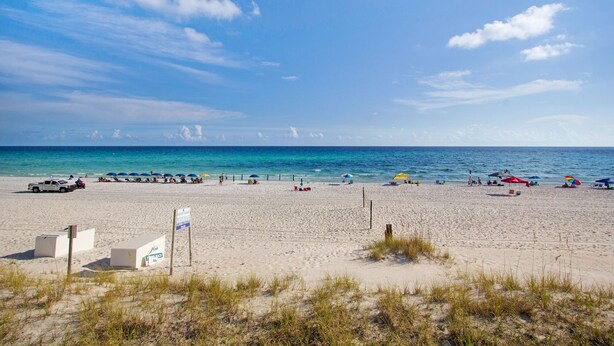 A beach with a white building, a sign, and a fence. -  Ariel Dunes l - Its Tannin' Time! - Fantastic Gulf Views! (Miramar Beach)