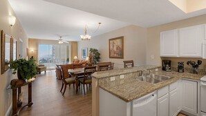 A modern kitchen with granite countertops, white cabinetry, and a dining area with a large table and chairs. -  Ariel Dunes l - Its Tannin' Time! - Fantastic Gulf Views! (Miramar Beach)