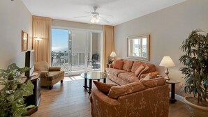 A living room with a sofa, a coffee table, a TV, and a balcony with a view. -  Ariel Dunes l - Its Tannin' Time! - Fantastic Gulf Views! (Miramar Beach)