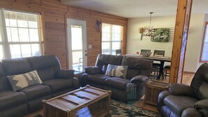 A cozy living room with a wooden floor, two leather sofas, a coffee table, and a patterned rug. - Riverfront Cabin! Mountain Views, Pool, Hot Tub, Fishing, Tubing, Fire Pit, WIFI (Hiawassee)