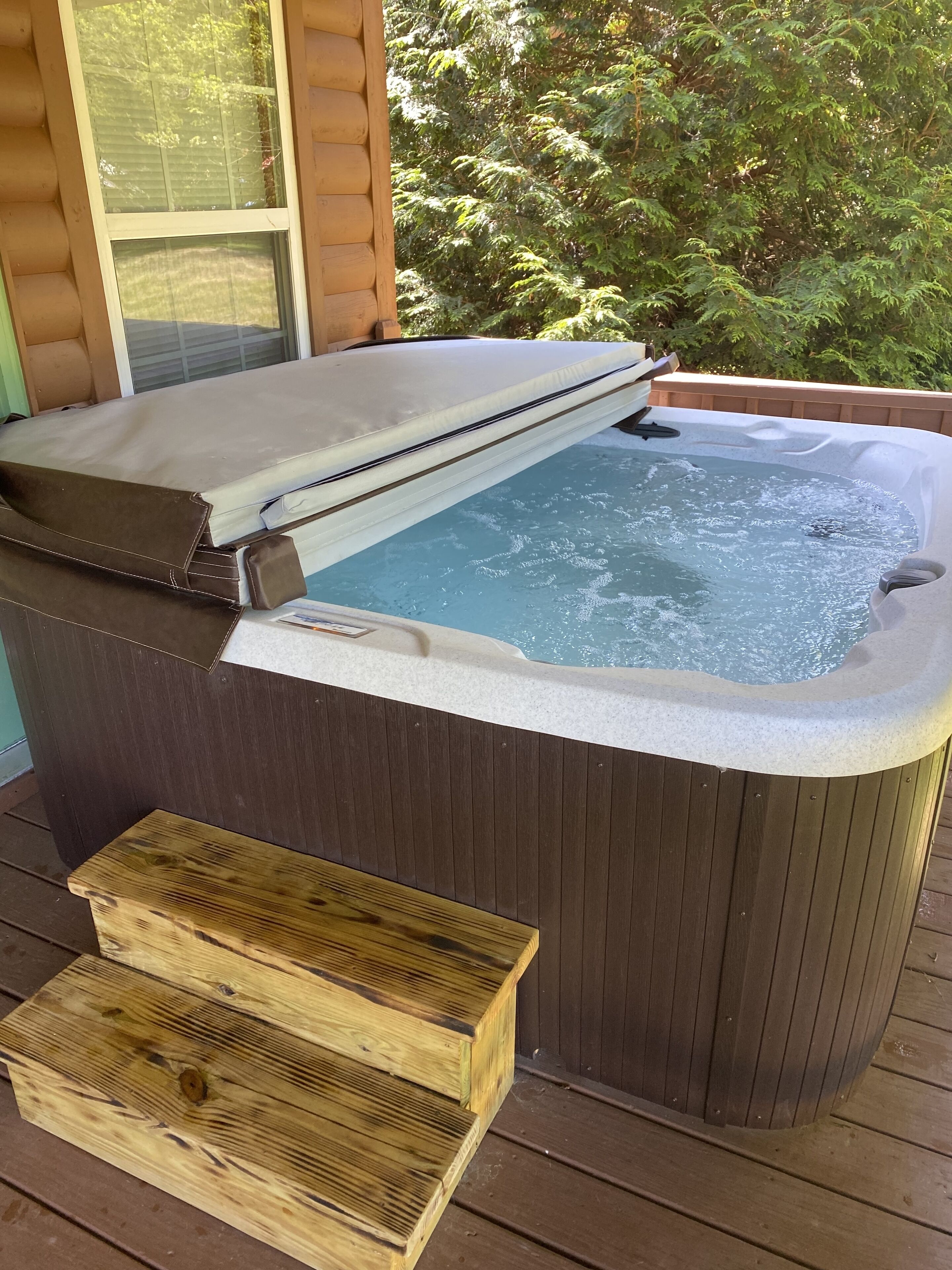 A hot tub with a wooden bench and a wooden box on a wooden deck.
